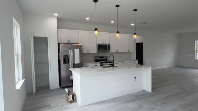 kitchen with appliances with stainless steel finishes, a center island with sink, white cabinets, pendant lighting, and sink