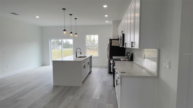 kitchen with a center island with sink, sink, white cabinetry, stainless steel appliances, and hanging light fixtures