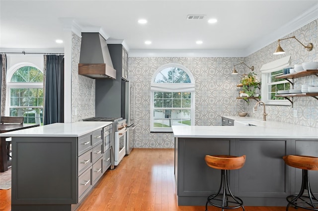 kitchen with wallpapered walls, open shelves, gray cabinetry, high end white range, and wall chimney exhaust hood