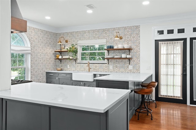 kitchen with open shelves, wallpapered walls, gray cabinets, a peninsula, and a sink