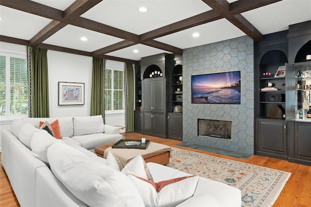 living area with a stone fireplace, light wood-style flooring, built in shelves, and coffered ceiling