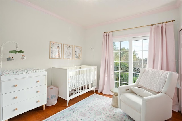 bedroom featuring a crib, wood finished floors, and crown molding