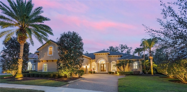 mediterranean / spanish-style house with decorative driveway, a lawn, and stucco siding