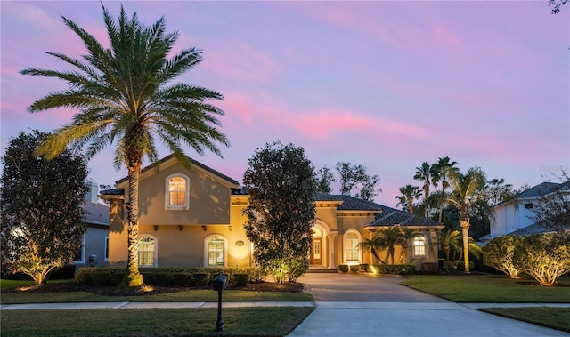 mediterranean / spanish house featuring decorative driveway, a lawn, a tiled roof, and stucco siding