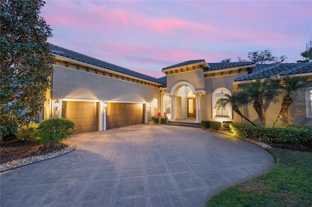 mediterranean / spanish-style home with decorative driveway, a tiled roof, an attached garage, and stucco siding