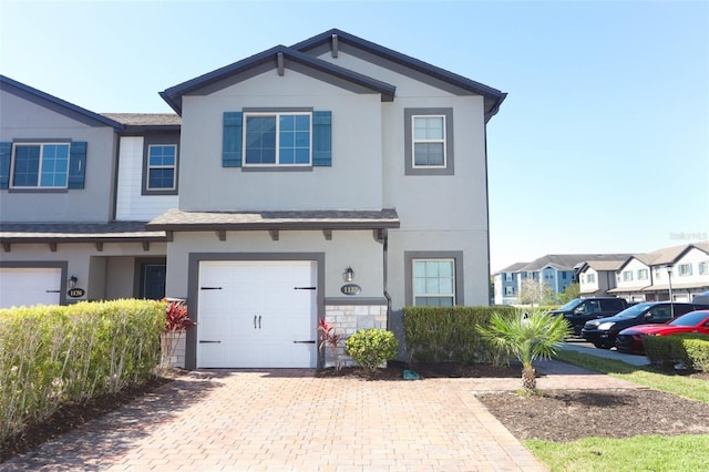 townhome / multi-family property featuring an attached garage, stone siding, decorative driveway, and stucco siding