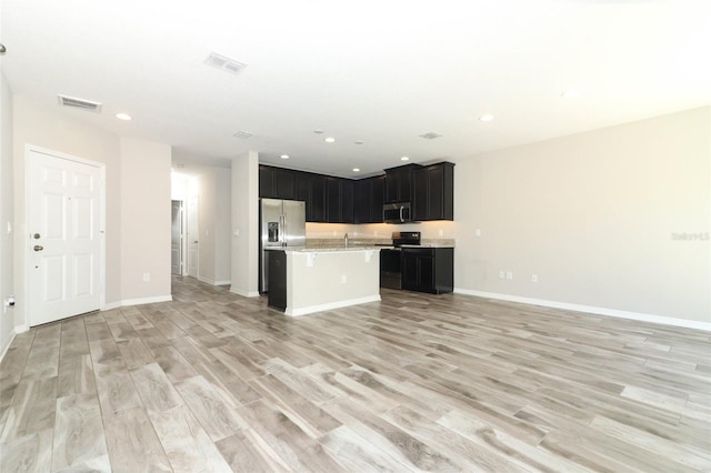 kitchen with a center island with sink, stainless steel appliances, light countertops, open floor plan, and dark cabinets