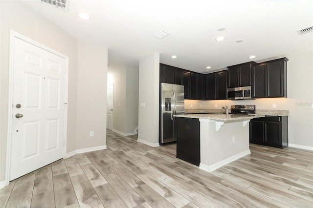 kitchen with visible vents, appliances with stainless steel finishes, a kitchen breakfast bar, light stone countertops, and a kitchen island with sink