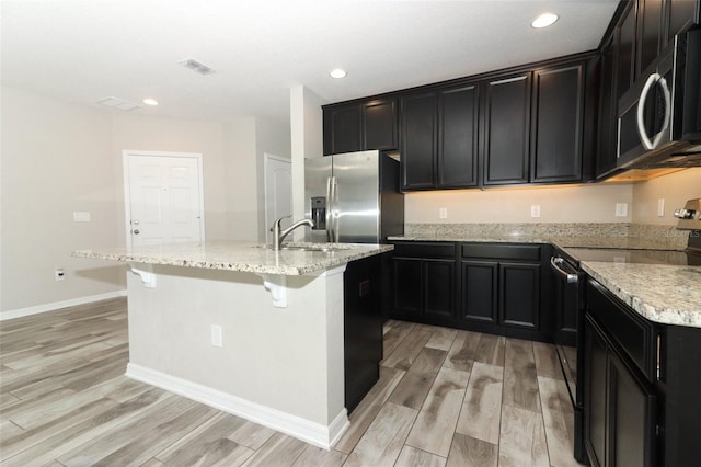 kitchen featuring stainless steel appliances, a sink, visible vents, a kitchen breakfast bar, and a center island with sink