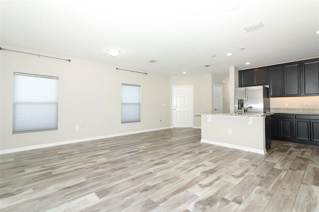 kitchen featuring light stone counters, a kitchen island with sink, a breakfast bar, open floor plan, and stainless steel fridge