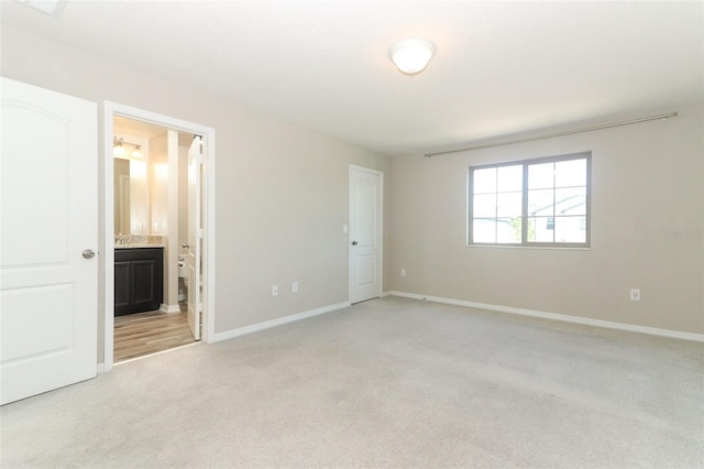 unfurnished bedroom featuring baseboards, ensuite bath, and light colored carpet