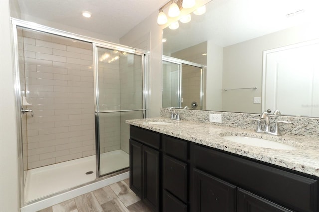 bathroom featuring double vanity, wood finished floors, a sink, and a shower stall