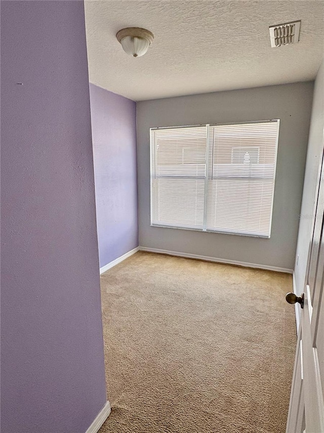 unfurnished room with a textured ceiling, carpet floors, visible vents, and baseboards