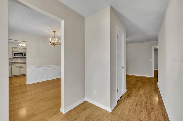 corridor featuring light wood-style floors, a notable chandelier, and baseboards