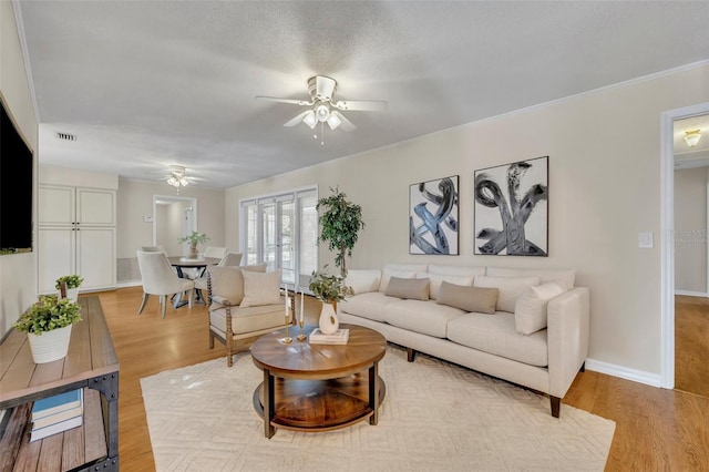 living area with ceiling fan, a textured ceiling, visible vents, baseboards, and light wood-style floors