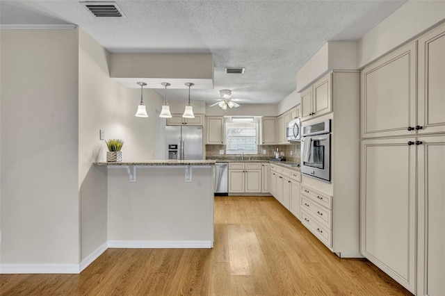 kitchen featuring a breakfast bar area, light wood finished floors, visible vents, appliances with stainless steel finishes, and a peninsula