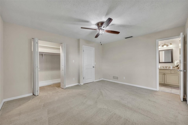 unfurnished bedroom featuring visible vents, light carpet, a textured ceiling, and baseboards