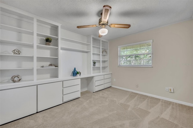 interior space featuring a textured ceiling, light carpet, a ceiling fan, baseboards, and built in study area