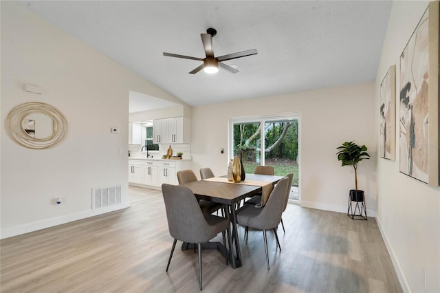 dining space with sink, ceiling fan, lofted ceiling, and light hardwood / wood-style floors