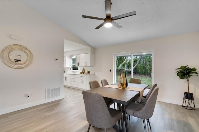 dining room with ceiling fan, sink, vaulted ceiling, and light wood-type flooring