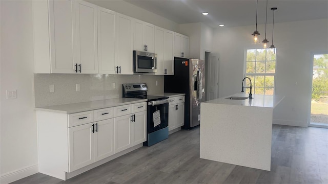 kitchen with a kitchen island with sink, stainless steel appliances, sink, white cabinets, and pendant lighting