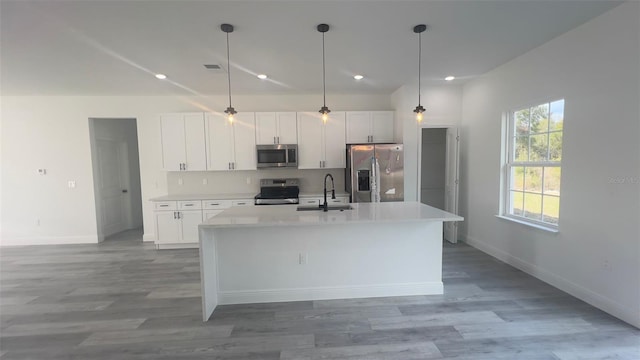 kitchen featuring appliances with stainless steel finishes, sink, decorative light fixtures, white cabinets, and an island with sink