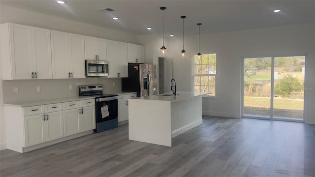 kitchen with sink, stainless steel appliances, white cabinets, hanging light fixtures, and a kitchen island with sink