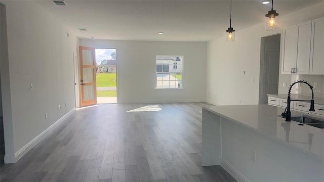 interior space with light stone countertops, light hardwood / wood-style floors, sink, white cabinets, and pendant lighting