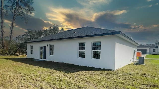 property exterior at dusk featuring a lawn and central AC