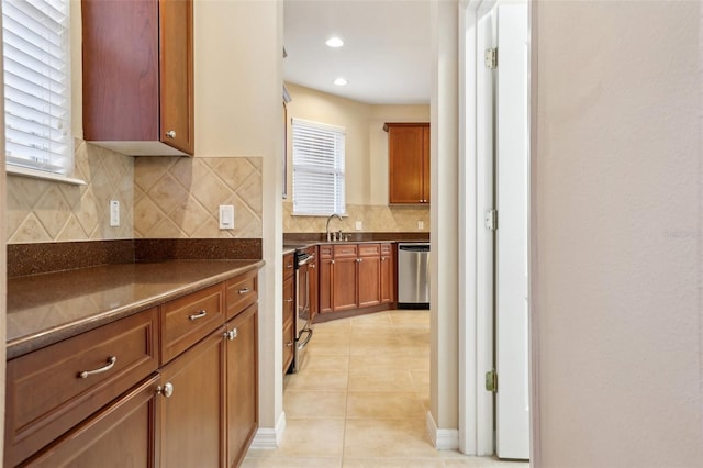 kitchen featuring stainless steel appliances, dark countertops, brown cabinetry, light tile patterned flooring, and a sink