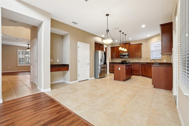 kitchen featuring dark countertops, a kitchen island, appliances with stainless steel finishes, open floor plan, and decorative light fixtures