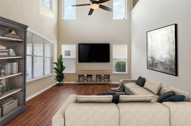 living room featuring ceiling fan, a high ceiling, baseboards, and dark wood-style flooring