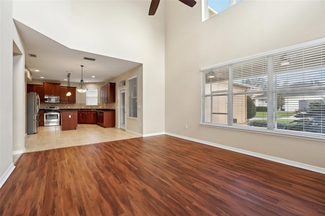 unfurnished living room with a wealth of natural light, light wood-style floors, visible vents, and baseboards