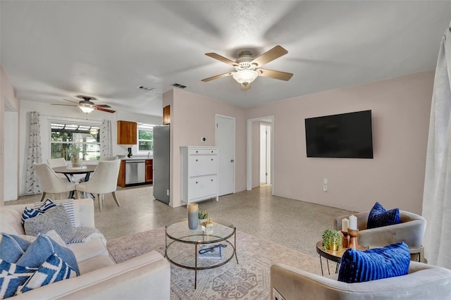 living area featuring light speckled floor, visible vents, and a ceiling fan