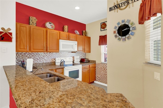 kitchen with light stone counters, a peninsula, white appliances, a sink, and backsplash