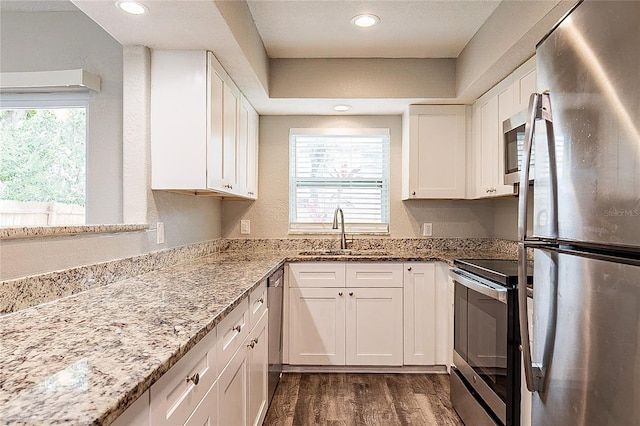 kitchen featuring dark wood finished floors, light stone counters, stainless steel appliances, white cabinetry, and a sink