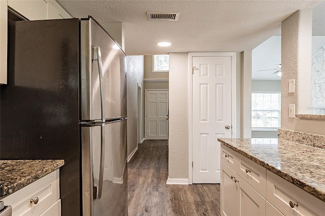 kitchen featuring visible vents, white cabinets, dark wood-type flooring, freestanding refrigerator, and a textured ceiling