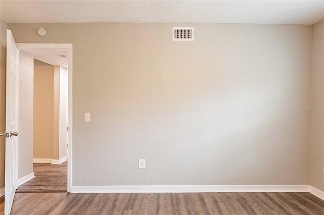 empty room with wood finished floors, visible vents, and baseboards