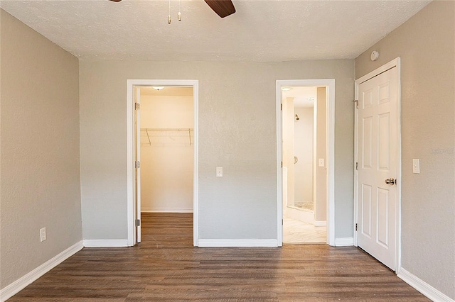 unfurnished bedroom featuring a spacious closet, wood finished floors, and baseboards