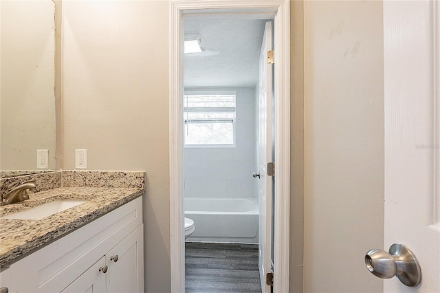 full bathroom with a textured ceiling, toilet, wood finished floors, vanity, and a bath