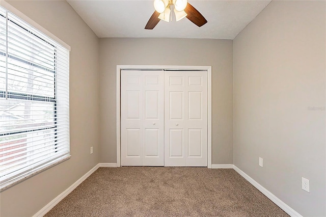 unfurnished bedroom with carpet floors, a closet, baseboards, and a ceiling fan