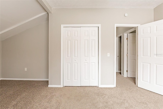 unfurnished bedroom with lofted ceiling with beams, a closet, baseboards, and carpet flooring