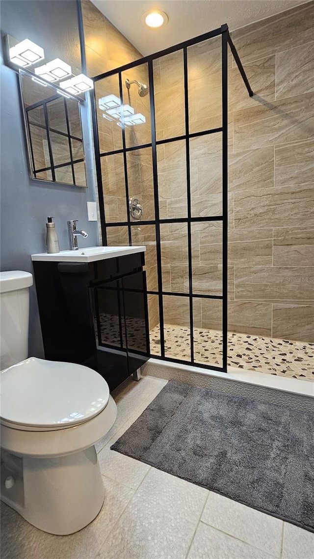 bathroom featuring a tile shower, vanity, tile patterned flooring, and toilet