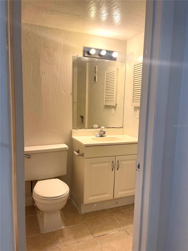 half bath with a textured wall, vanity, toilet, and tile patterned floors