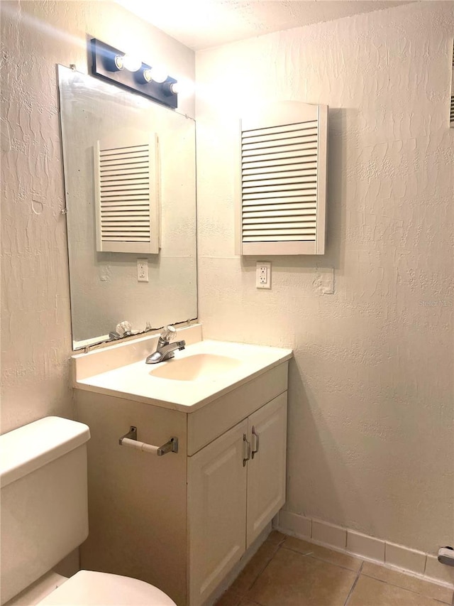 bathroom with a textured wall, toilet, vanity, baseboards, and tile patterned floors