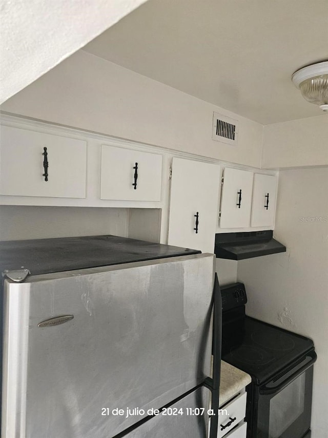 kitchen featuring visible vents, white cabinetry, under cabinet range hood, black / electric stove, and stainless steel refrigerator