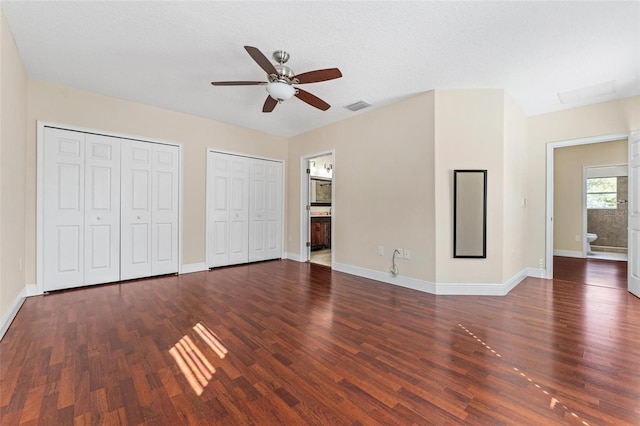 unfurnished bedroom featuring dark wood-type flooring, two closets, and visible vents