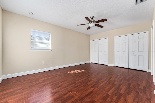 unfurnished bedroom featuring baseboards, visible vents, dark wood finished floors, and two closets