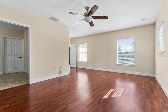 unfurnished room featuring a textured ceiling, wood finished floors, a ceiling fan, visible vents, and baseboards