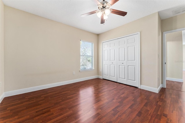 unfurnished bedroom with dark wood-type flooring, a ceiling fan, visible vents, baseboards, and a closet